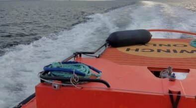 Orange rescue boat with coiled rope on deck, speeding across choppy sea toward the horizon under cloudy sky