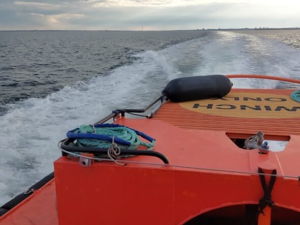 Orange rescue boat with coiled rope on deck, speeding across choppy sea toward the horizon under cloudy sky
