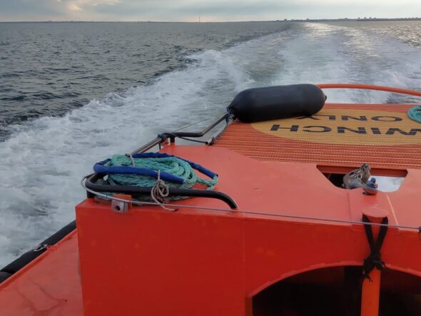 Orange rescue boat with coiled rope on deck, speeding across choppy sea toward the horizon under cloudy sky