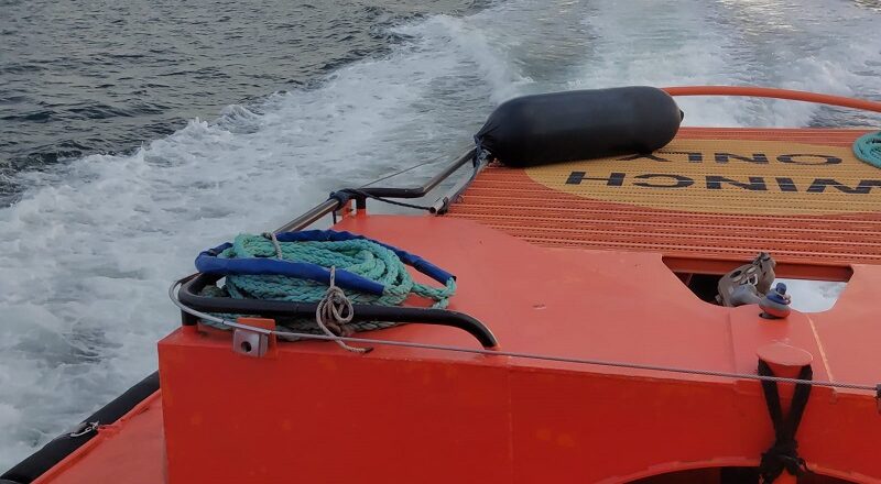 Orange rescue boat with coiled rope on deck, speeding across choppy sea toward the horizon under cloudy sky