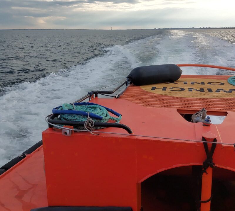 Orange rescue boat with coiled rope on deck, speeding across choppy sea toward the horizon under cloudy sky