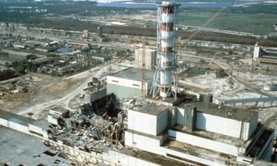 Industrial ruin: shattered buildings and scattered debris around a damaged power plant site with a tall striped lattice tower in the foreground.