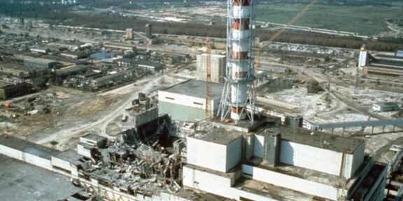 Industrial ruin: shattered buildings and scattered debris around a damaged power plant site with a tall striped lattice tower in the foreground.