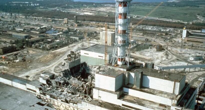 Industrial ruin: shattered buildings and scattered debris around a damaged power plant site with a tall striped lattice tower in the foreground.