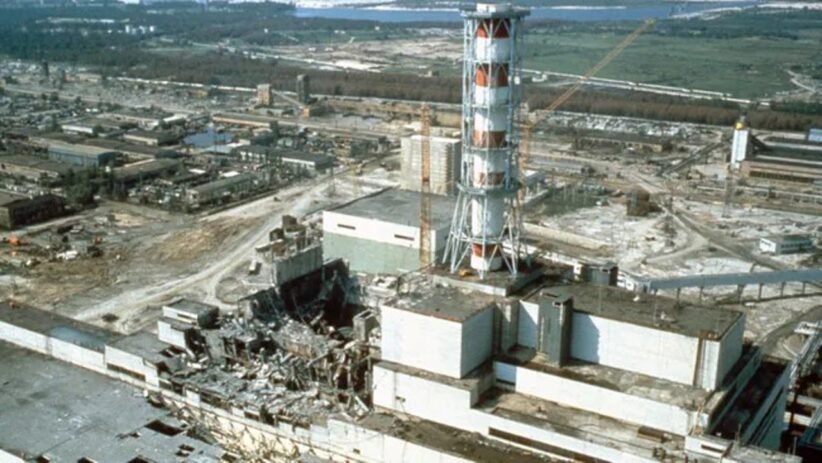 Industrial ruin: shattered buildings and scattered debris around a damaged power plant site with a tall striped lattice tower in the foreground.
