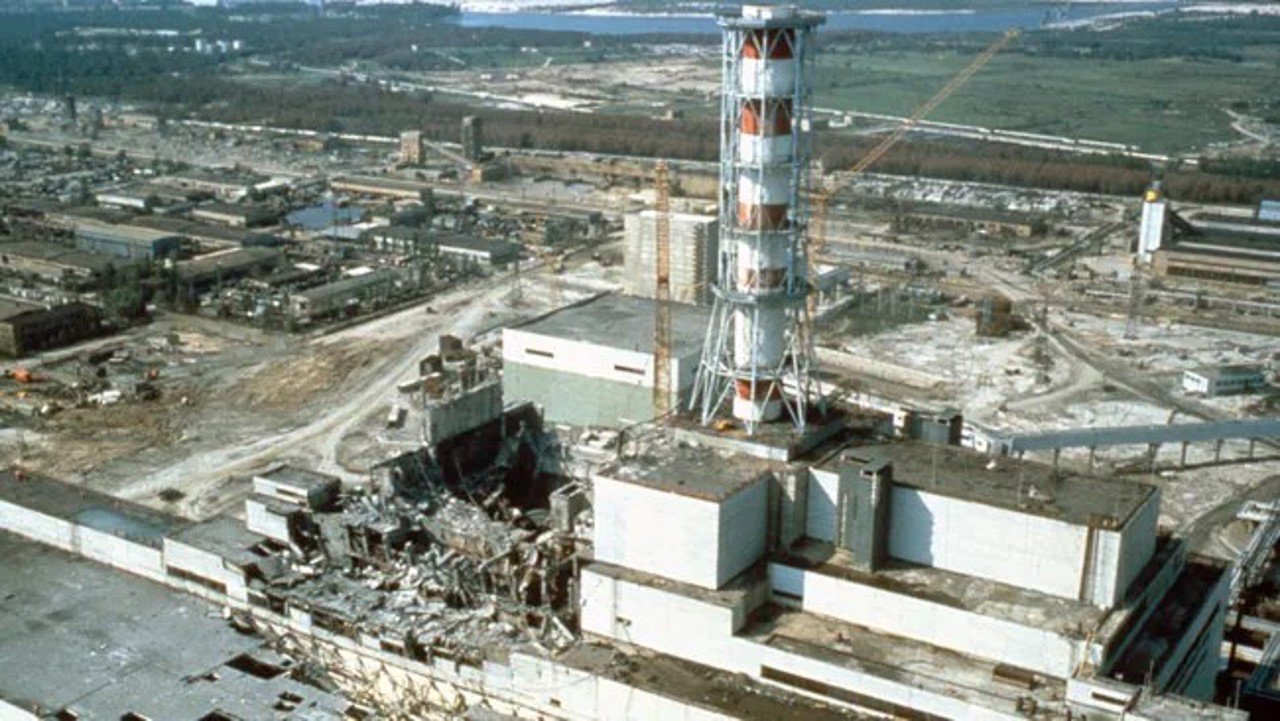 Industrial ruin: shattered buildings and scattered debris around a damaged power plant site with a tall striped lattice tower in the foreground.
