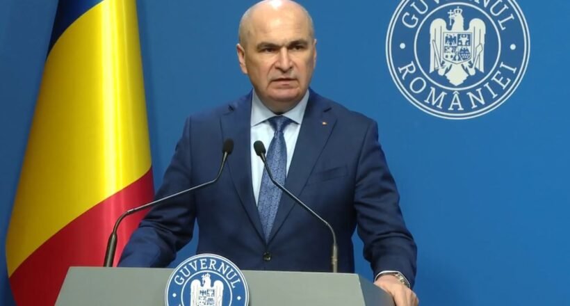 Romanian official giving a press conference at a podium, with national flag and government seal in the background.