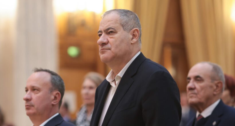 Middle-aged man in a dark suit standing at a formal event, with others in the background.