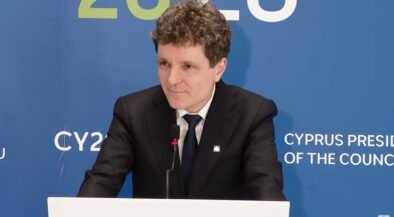Man in a black suit and tie giving a speech at a podium, with a blue backdrop that reads 'Cyprus Presidency of the Council'.