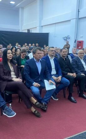 Group of professionally dressed people seated in rows at an indoor conference or seminar hall.