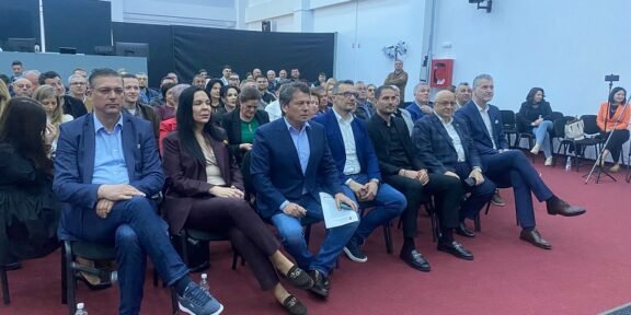Group of professionally dressed people seated in rows at an indoor conference or seminar hall.