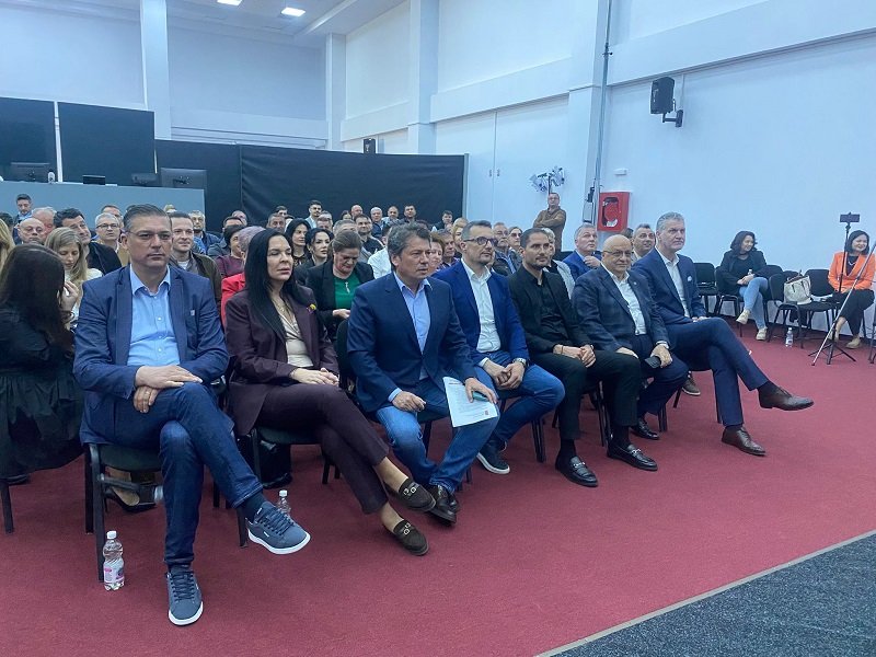 Group of professionally dressed people seated in rows at an indoor conference or seminar hall.
