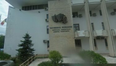 Front view of a Romanian government building with a stone pillar and emblem, the sign reading 'Guvernul României' and 'Constanța'
