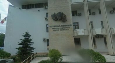 Front view of a Romanian government building with a stone pillar and emblem, the sign reading 'Guvernul României' and 'Constanța'