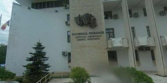 Front view of a Romanian government building with a stone pillar and emblem, the sign reading 'Guvernul României' and 'Constanța'