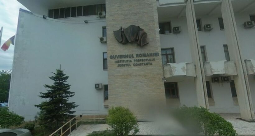 Front view of a Romanian government building with a stone pillar and emblem, the sign reading 'Guvernul României' and 'Constanța'