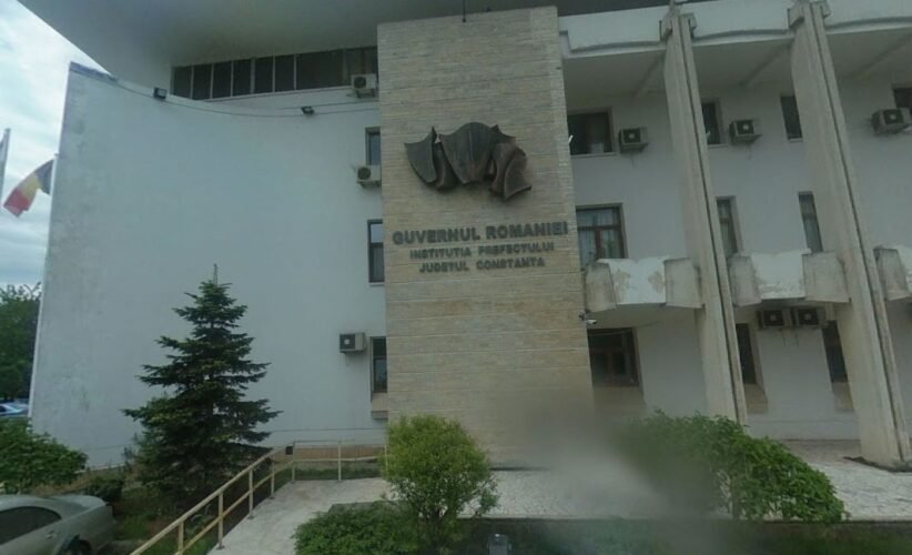 Front view of a Romanian government building with a stone pillar and emblem, the sign reading 'Guvernul României' and 'Constanța'