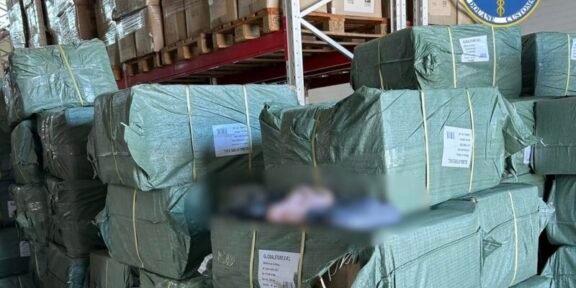 Stacks of green-wrapped bundles on wooden pallets in a warehouse, with a Romanian customs logo visible in the top right corner and labels on the bundles.