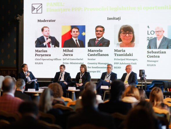 Panel discussion on PPP financing is taking place on a stage with a moderator and five panelists seated in front of a large screen showing their photos and names; audience watches from the foreground.