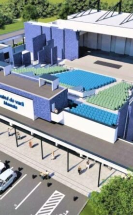 A rendered aerial view of a modern sports arena with blue and green seating, a large entrance, and a parking lot nearby.