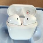 White wireless earbuds in their open charging case resting on a light blue surface, viewed from above.Apple AirPods in case ready to use.