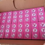 Open cardboard box filled with 24 pink boxes, each featuring a white circular logo, arranged in a neat grid.