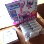 Pink kids' toy box with cartoon creatures and a pink activity table, beside a plastic-wrapped set of white discs.