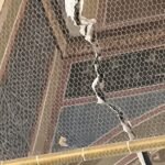 Large ceiling crack with torn plaster and exposed wire mesh/reinforcement, showing structural damage behind the surface area, indoors.