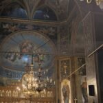 Interior of a richly decorated Orthodox church with a gilded iconostasis, chandeliers, and a crowd gathered for a service.