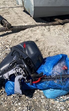 Outboard boat motor lying on rocky ground, wrapped in a blue tarp with tangled lines nearby.