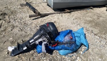 Outboard boat motor lying on rocky ground, wrapped in a blue tarp with tangled lines nearby.