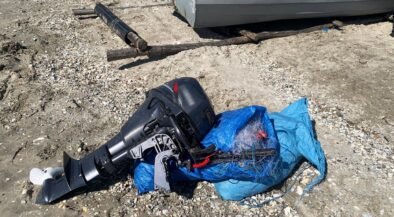 Outboard boat motor lying on rocky ground, wrapped in a blue tarp with tangled lines nearby.