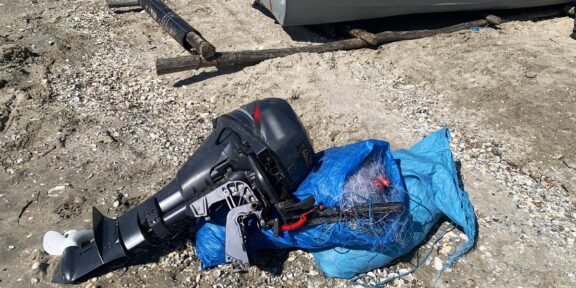 Outboard boat motor lying on rocky ground, wrapped in a blue tarp with tangled lines nearby.