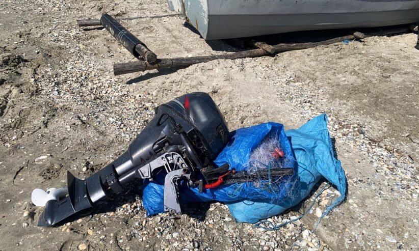 Outboard boat motor lying on rocky ground, wrapped in a blue tarp with tangled lines nearby.