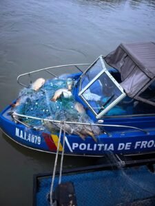 Blue police boat loaded with tangled fishing nets and buoys on its deck, near calm water.