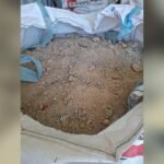 Loose brown soil and small rocks inside an open white woven bag, edge visible at the bottom of the frame.