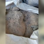 Pile of brown soil/semi-dry dirt spilling from a white woven bag, showing loose clumps and fine dust.