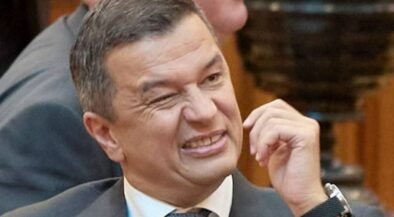 Man in a suit grimaces while rubbing his cheek at a meeting conference room scene.