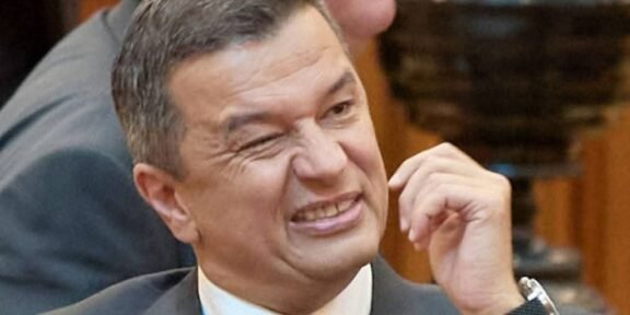 Man in a suit grimaces while rubbing his cheek at a meeting conference room scene.