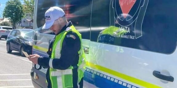 Policeman in a bright vest stands beside a blue-and-white police van, looking at a handheld device.