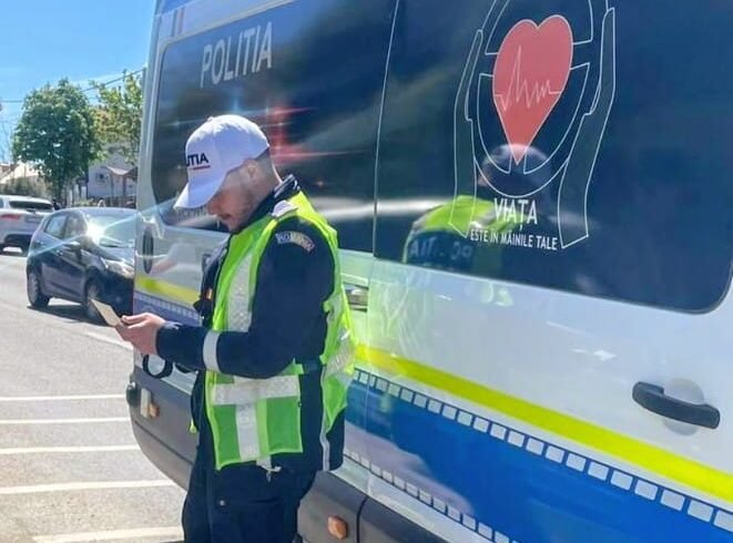 Policeman in a bright vest stands beside a blue-and-white police van, looking at a handheld device.
