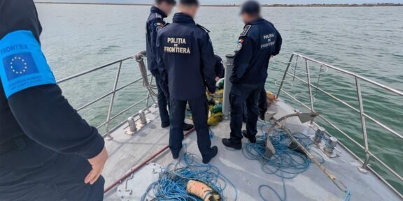 Border police officers on a boat by the water, examining nets and blue ropes on deck.