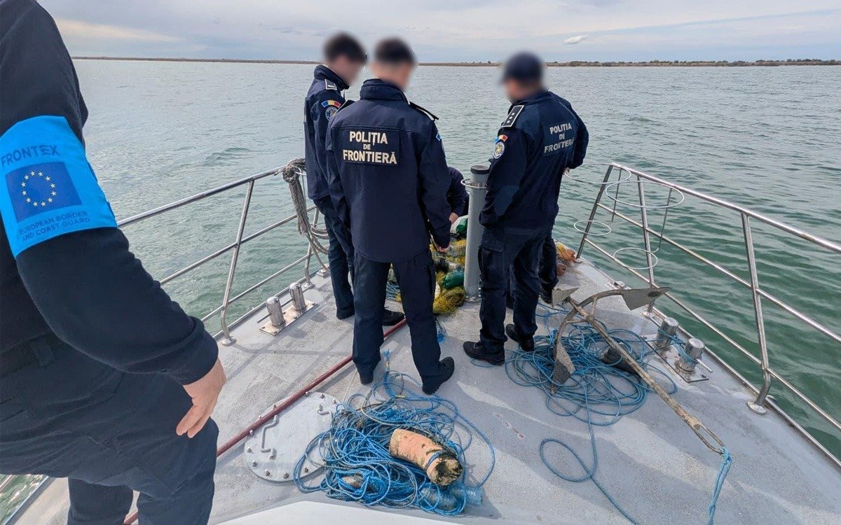 Border police officers on a boat by the water, examining nets and blue ropes on deck.