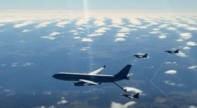 Large military tanker aircraft refuels a fighter jet in mid-air, with other jets nearby over a partly cloudy sky.