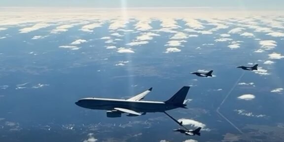 Large military tanker aircraft refuels a fighter jet in mid-air, with other jets nearby over a partly cloudy sky.