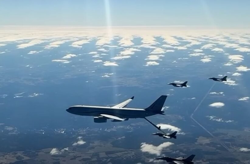 Large military tanker aircraft refuels a fighter jet in mid-air, with other jets nearby over a partly cloudy sky.