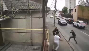 Group of men in a street confrontation on a sidewalk as cars drive by on a city road.