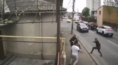 Group of men in a street confrontation on a sidewalk as cars drive by on a city road.