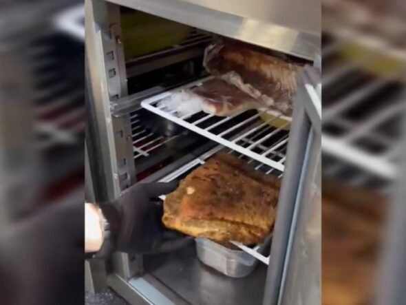 Person in a black glove lifts a large browned roast from a metal smoker/oven rack.