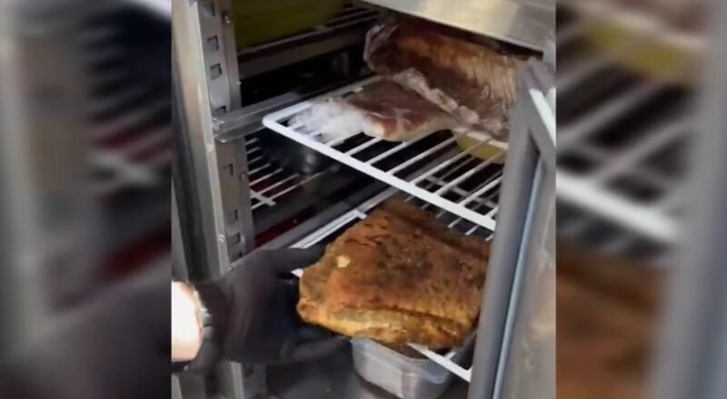 Person in a black glove lifts a large browned roast from a metal smoker/oven rack.